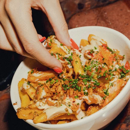 a manicured hand grabbing some loaded fries from a plate